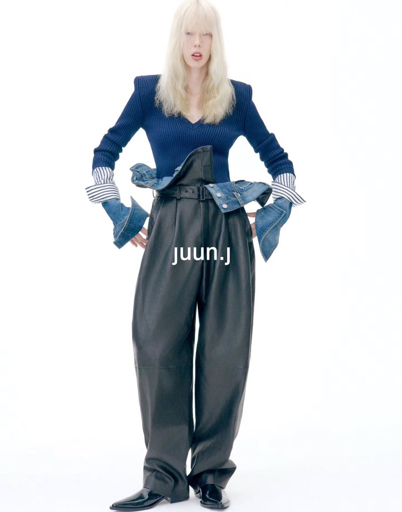 Model with blonde hair wearing a blue top and black leather trousers against a white background