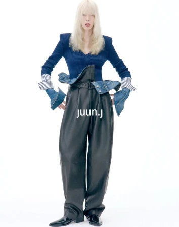 Model with blonde hair wearing a blue top and black leather trousers against a white background