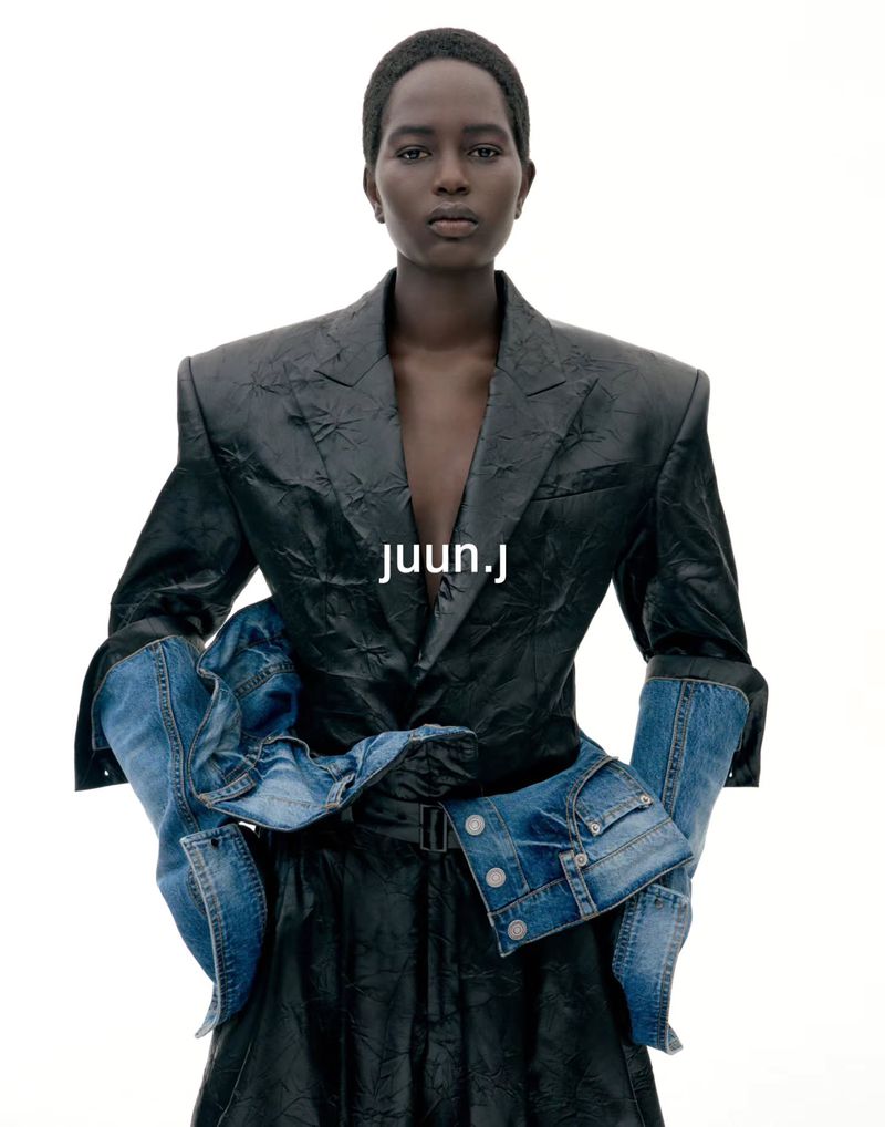Model with short hair wearing a black leather blazer and denim sleeves against a white background