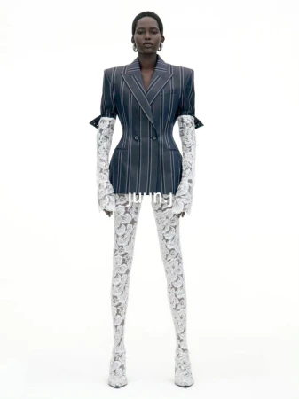 Model standing against a white seamless background wearing a pinstriped blazer and white lace sleeves