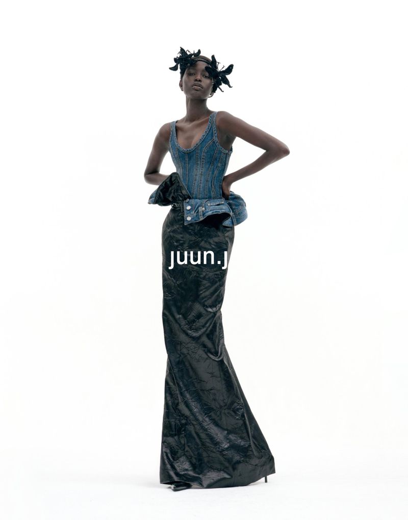 Model wearing a blue denim corset top and dark maxi skirt against a white background for Juun.J S/S27