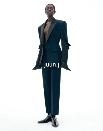 Model wearing dark structured blazer and matching trousers against plain white seamless background