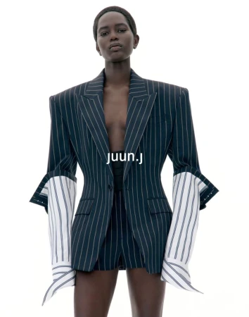 Model wearing a dark pinstripe structured blazer with extended white shirt cuffs against a stark white background.
