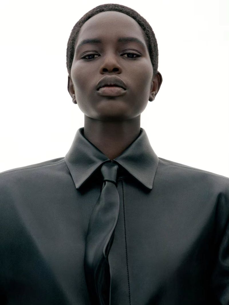Portrait of a model wearing a dark leather shirt and tie against a plain white background for Juun.J S/S27