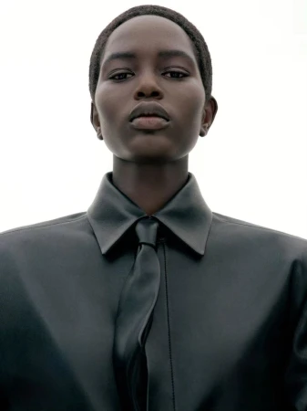 Portrait of a model wearing a dark leather shirt and tie against a plain white background for Juun.J S/S27