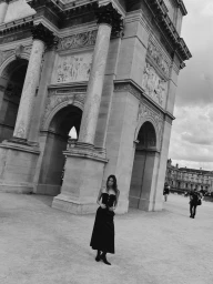 Monochrome fashion portrait of a model in a dark strapless dress standing before a massive neoclassical archway.