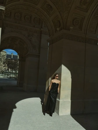 Model in a black strapless dress standing beneath grand neoclassical archways in bright natural sunlight.