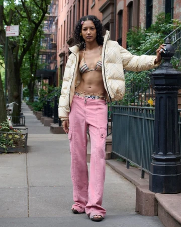 Woman in cream puffer jacket and pink pants standing on a city sidewalk