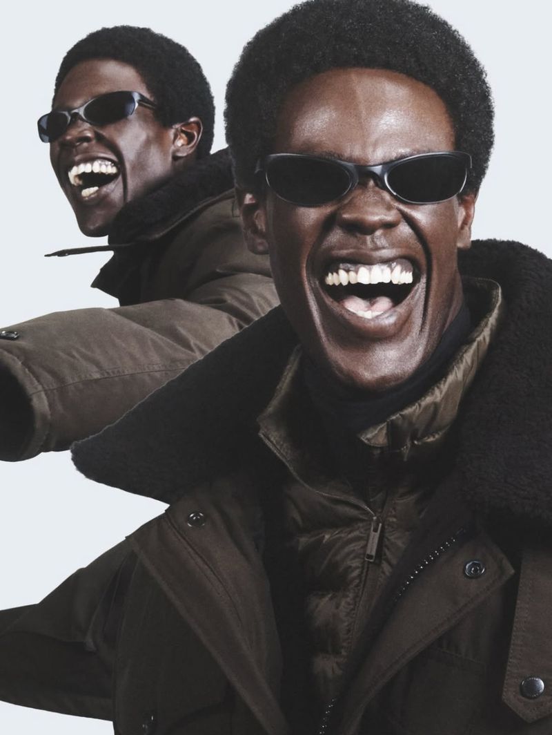 Two black men smiling in winter parkas and sunglasses against a white background