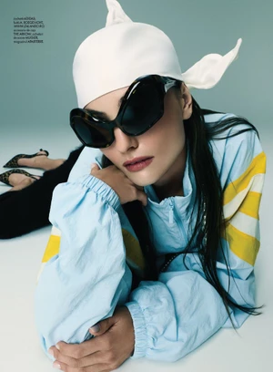 Model wearing a white headscarf, oversized sunglasses, and a light blue tracksuit posing against a pale background