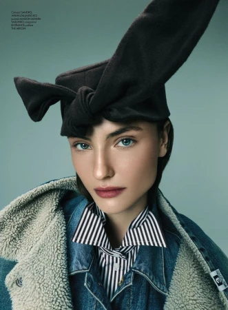 Model wearing a black knotted hat, striped shirt, and denim jacket with shearling lining against a teal background.