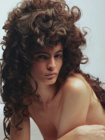 Portrait of a woman with voluminous dark curly hair and neutral expression against a plain white background