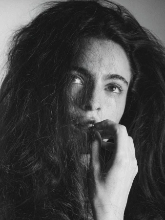 Monochrome portrait of a woman with dark wavy hair gently holding strands near her lips against a neutral background.