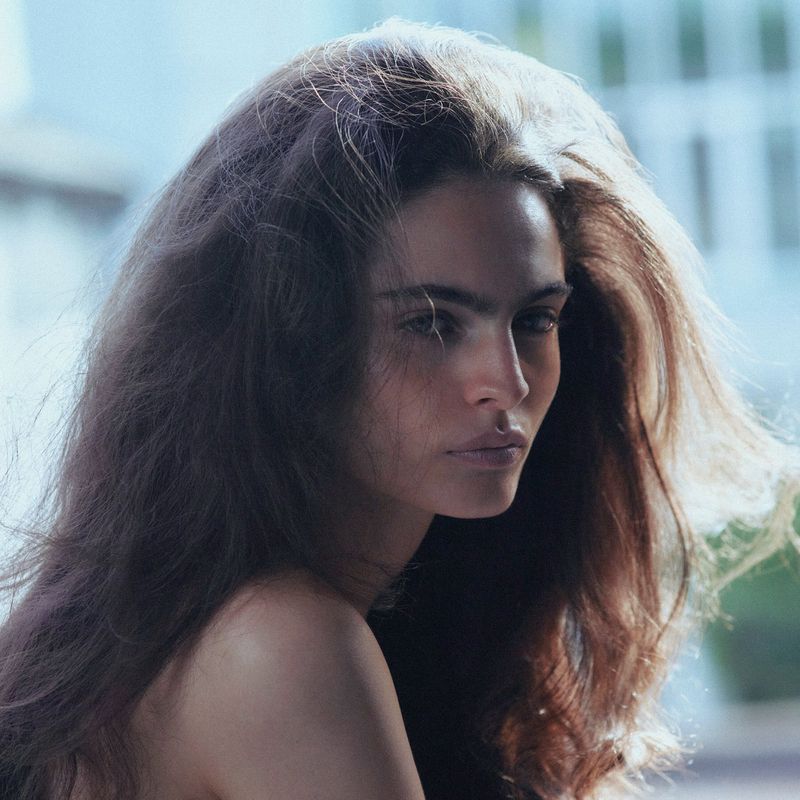 Close-up portrait of a woman with voluminous dark brown hair and soft backlighting for i-D Magazine