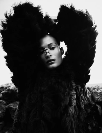 Model wearing a dark textured faux fur coat with arms raised against an outdoor rocky background