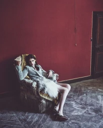 Model wearing grey tweed jacket seated in an armchair against a rich red wall for Harper's Bazaar Italia