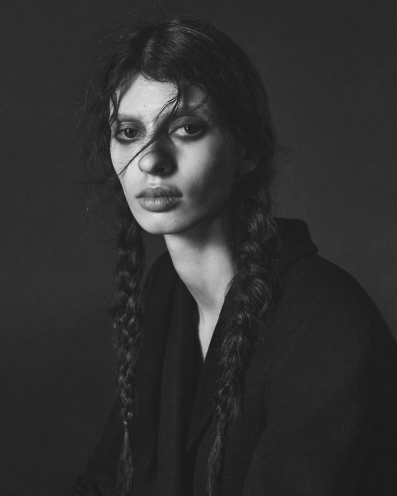 Portrait of a model with braided hair wearing a dark jacket against a dark background for Harper's Bazaar Italia