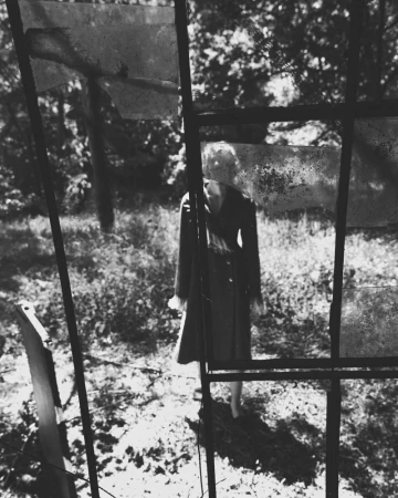 Model viewed through a broken industrial window frame outdoors in a wooded area for Harper's Bazaar Italia