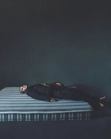 Model lying on a striped mattress against a dark textured background in an editorial fashion photograph.
