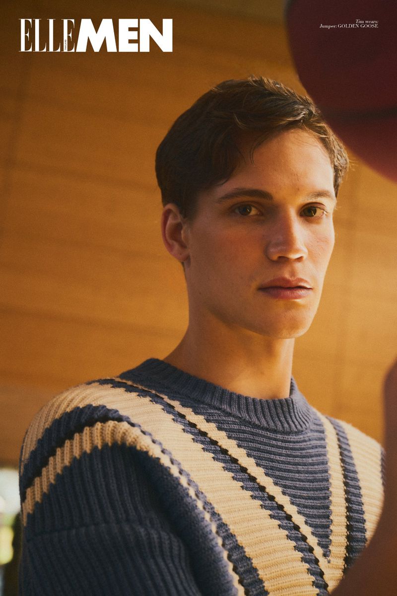 Portrait of a young man wearing a striped blue and cream knit sweater against a warm wood-paneled interior for Elle Men Thailand.