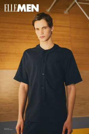 Model wearing dark pinstriped short sleeve button shirt against wooden wall background