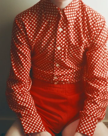 Person wearing a red and white polka dot button-down shirt paired with red shorts against a plain background.