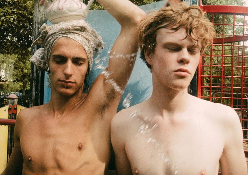 Two shirtless young men outdoors with water splashing while one holds a ceramic teapot overhead for Office Magazine.