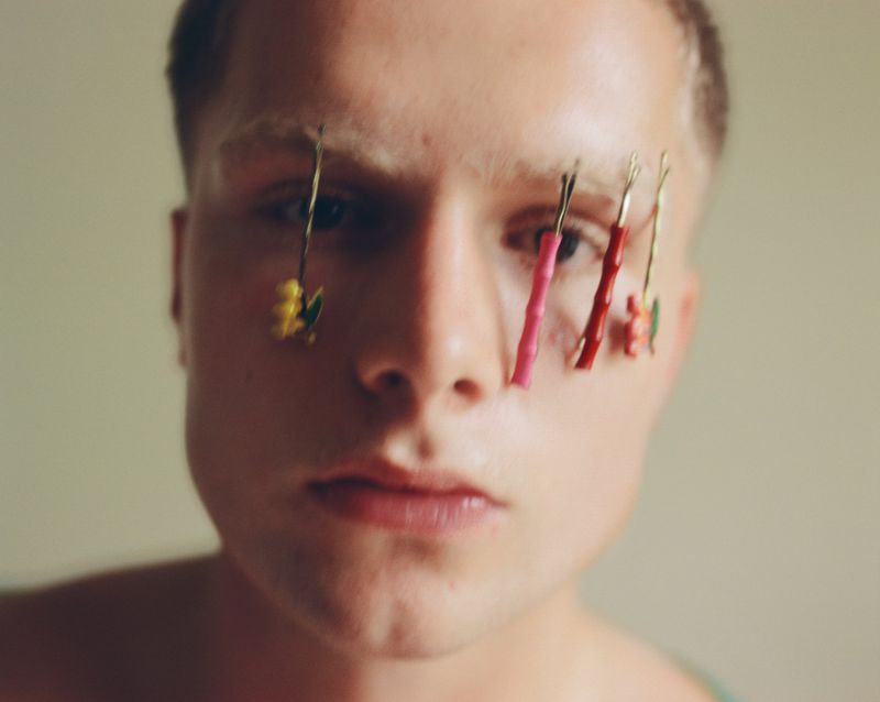 Close-up portrait of a young man with colorful hair clips pinned vertically over his eyebrows for Office Magazine.