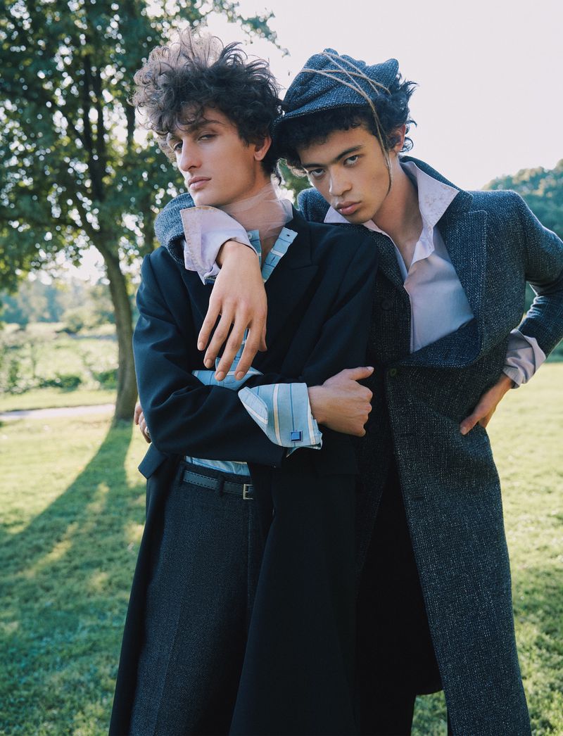Two male models posing together outdoors on a grassy lawn with trees in the background for a Flaunt magazine fashion editorial.