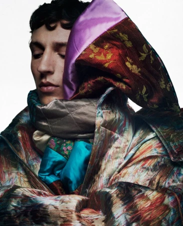 Close-up portrait of a male model wrapped in a vibrant patterned and quilted fabric coat with satin lining against a plain white background