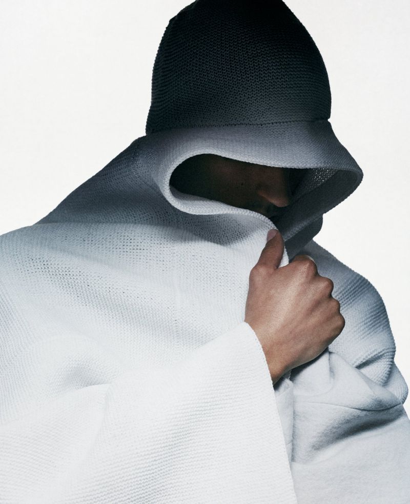Model wearing a dark beanie and white hooded garment wrapped tightly around the head against a plain white background