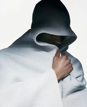 Model wearing a dark beanie and white hooded garment wrapped tightly around the head against a plain white background