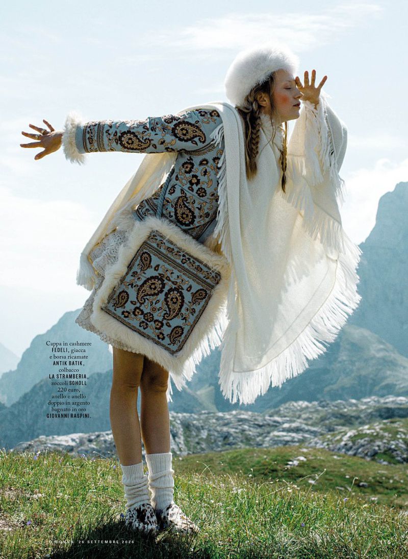 Model in patterned jacket and white fur hat posing outdoors in a mountainous landscape for iO Donna