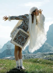 Model in patterned jacket and white fur hat posing outdoors in a mountainous landscape for iO Donna