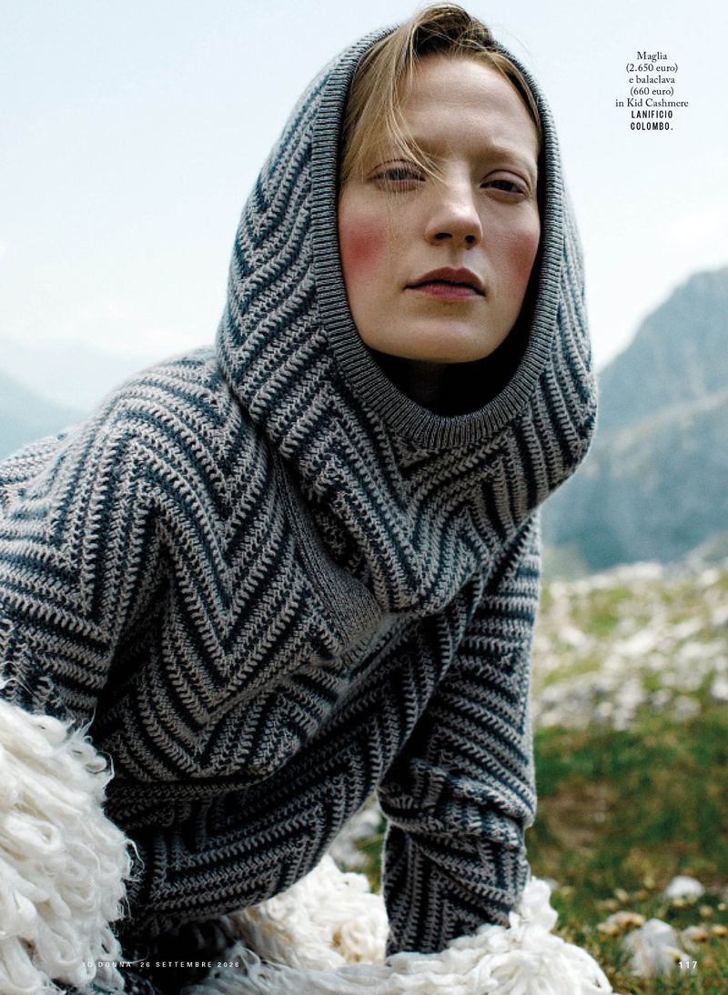Model wearing a grey knitted hooded sweater outdoors in a mountainous landscape for iO Donna editorial