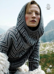 Model wearing a grey knitted hooded sweater outdoors in a mountainous landscape for iO Donna editorial