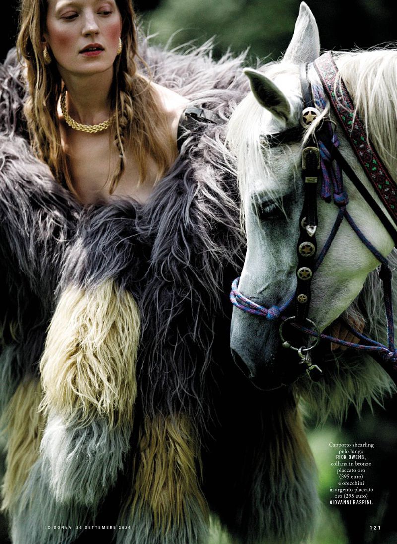 Model wearing a textured fluffy gray and yellow coat next to a white horse in an outdoor setting