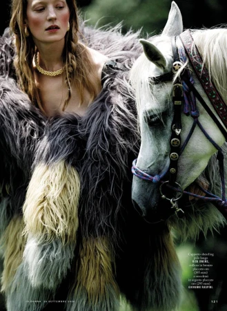 Model wearing a textured fluffy gray and yellow coat next to a white horse in an outdoor setting