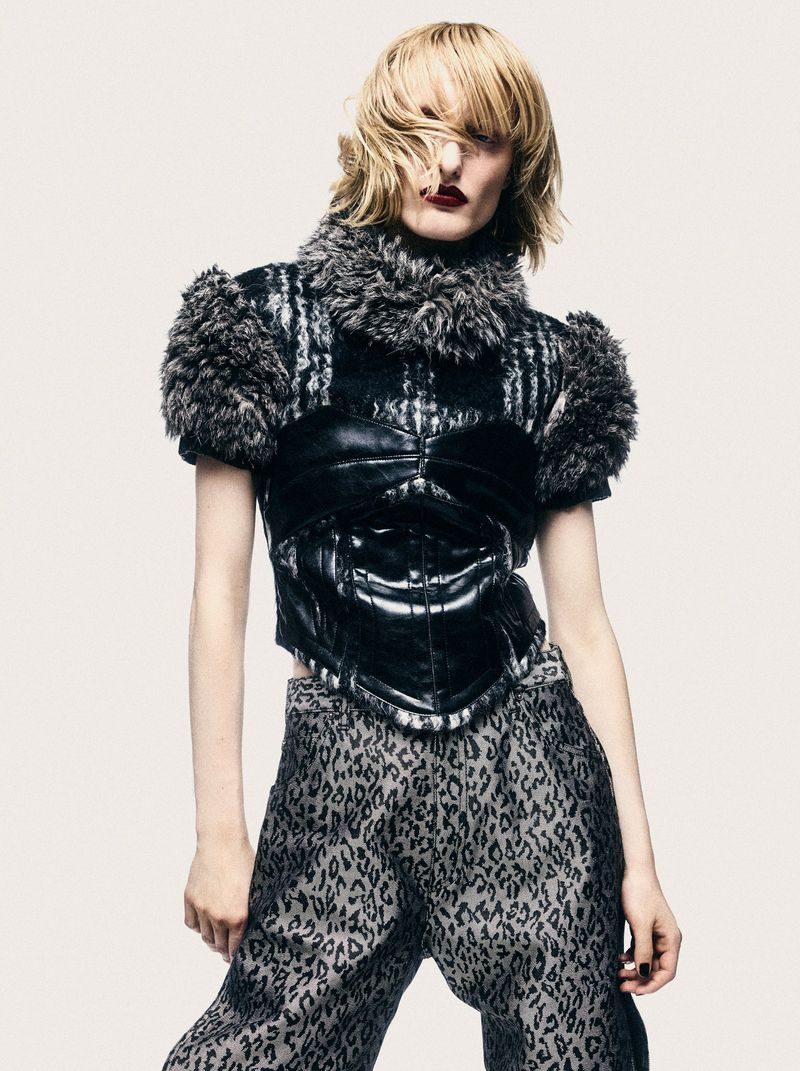 Model with blonde hair and dark lipstick wearing a patterned top with fur collar and leopard print pants