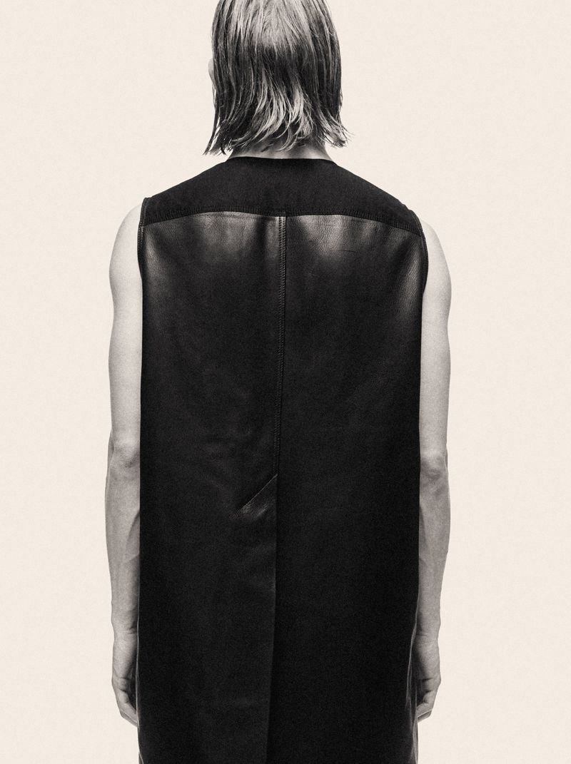 Model seen from behind wearing a black leather sleeveless top against a pale cream background