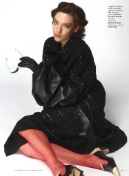 Model seated on white background wearing a black sequined coat, black leather gloves, red tights, and holding sunglasses.