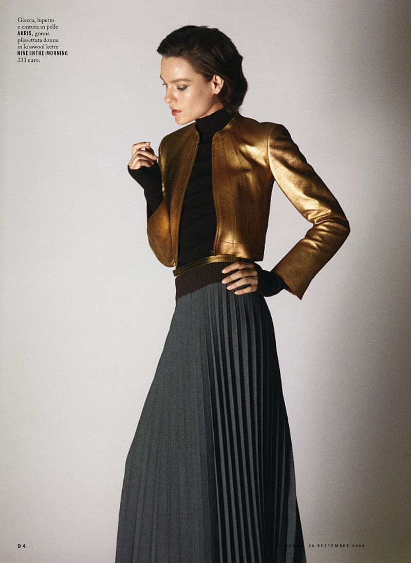 Model wearing a gold metallic jacket and a pleated grey skirt against a neutral background for iO Donna.