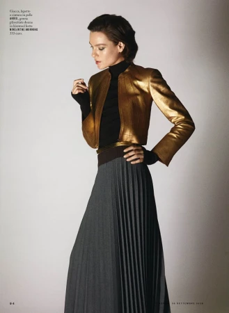 Model wearing a gold metallic jacket and a pleated grey skirt against a neutral background for iO Donna.