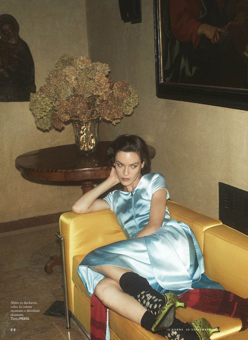 Model seated on a yellow armchair in a classic interior wearing a light blue dress with black socks and patterned heels