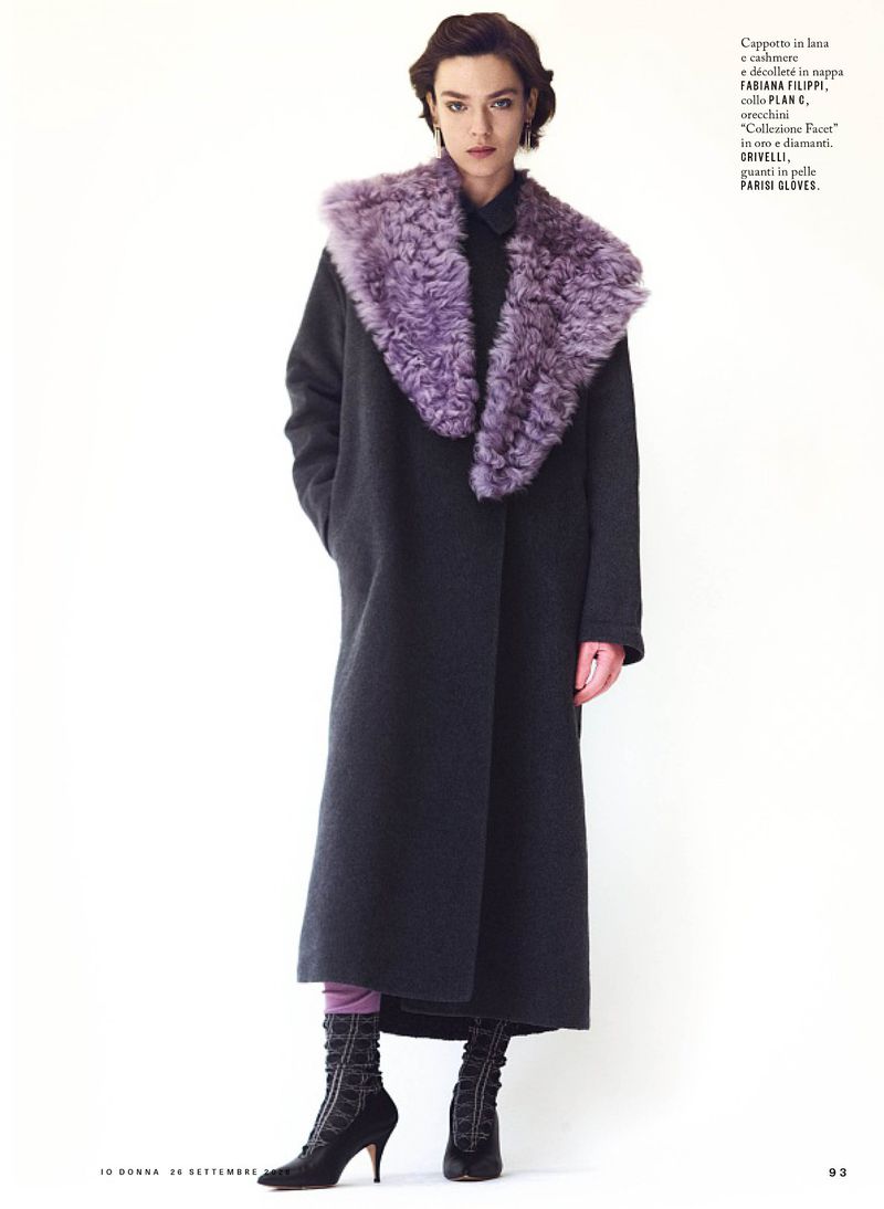 Model wearing a dark long coat with a prominent purple fur collar against a plain white background