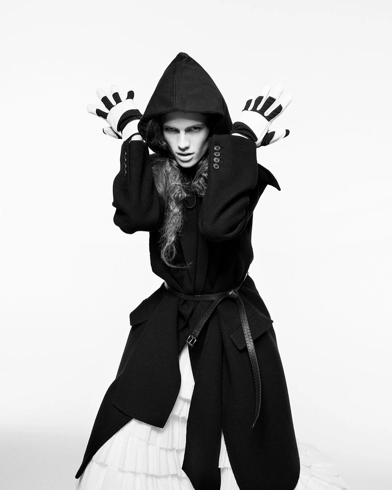 Model in a black hooded coat and striped gloves posing against a plain white background for D Repubblica.