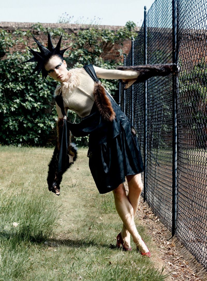 Model with spiked hair wearing dark outfit leaning against a wire fence outdoors in a D Repubblica fashion editorial.