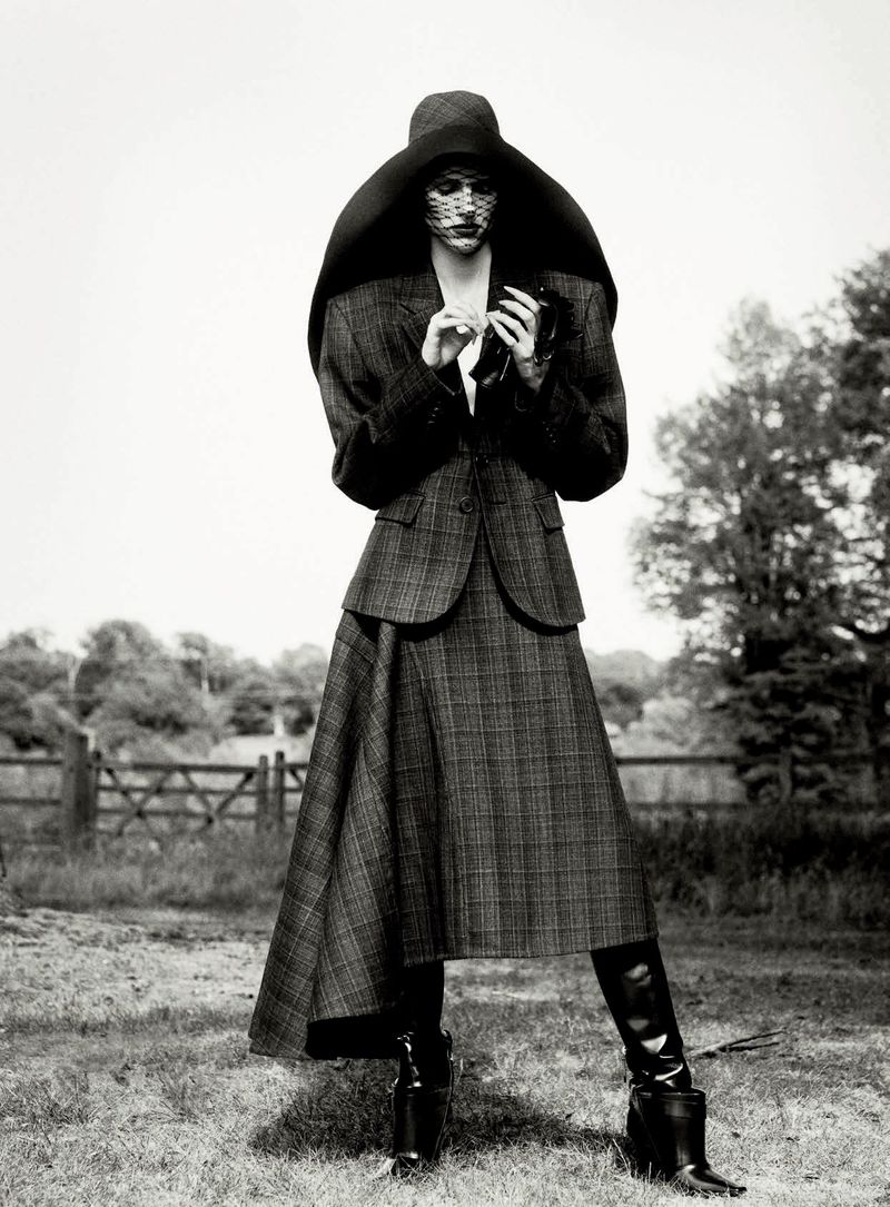 Model in plaid skirt suit and oversized wide-brim hat standing outdoors for D Repubblica