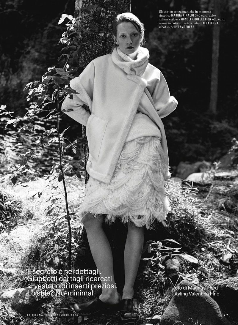 Model Marie Louwes in a white fluffy coat and fringe skirt leaning against a tree in a forest for iO Donna