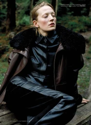 Model wearing a dark leather jacket with a fur collar and leather trousers in a forest setting for iO Donna project Wild